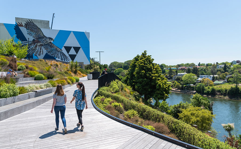 Two women walk along a decked promenade next to the Waikato River in central Hamilton, Waikato, New Zealand